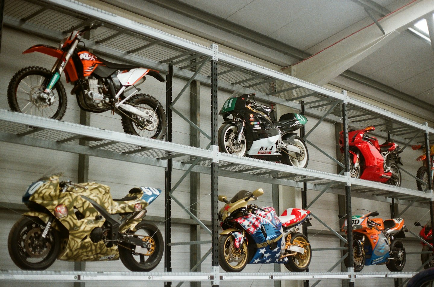 Różne motocykle zaparkowane na metalowych stojakach magazynowych w magazynie.